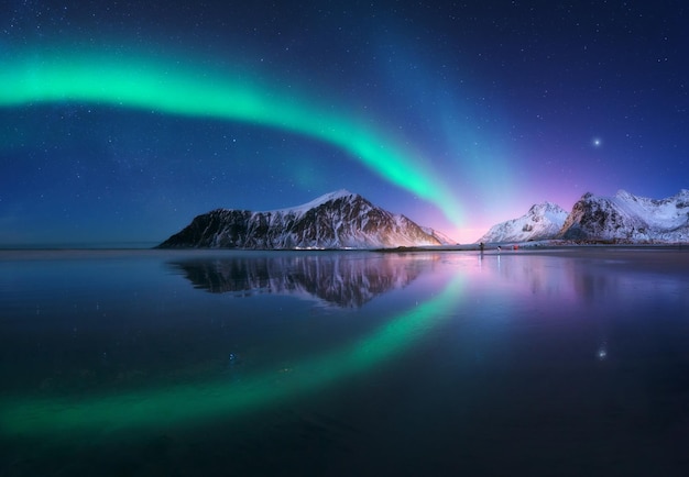 Aurora boreal e praia nas ilhas Lofoten, Noruega Belas luzes do norte Céu estrelado com luzes polares Paisagem noturna de inverno com mar aurora com reflexo do céu luzes da cidade montanhas nevadas