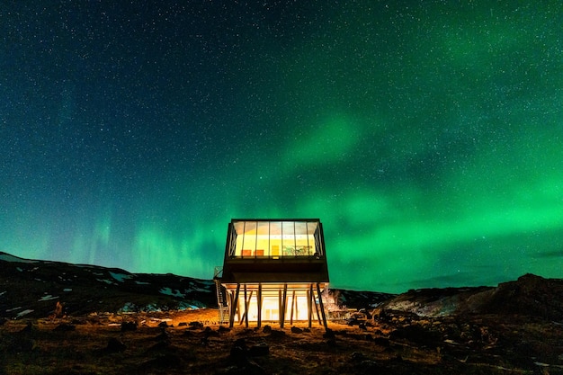 Foto aurora boreal las luces del norte brillan sobre un hotel de lujo en el desierto volcánico en invierno en islandia