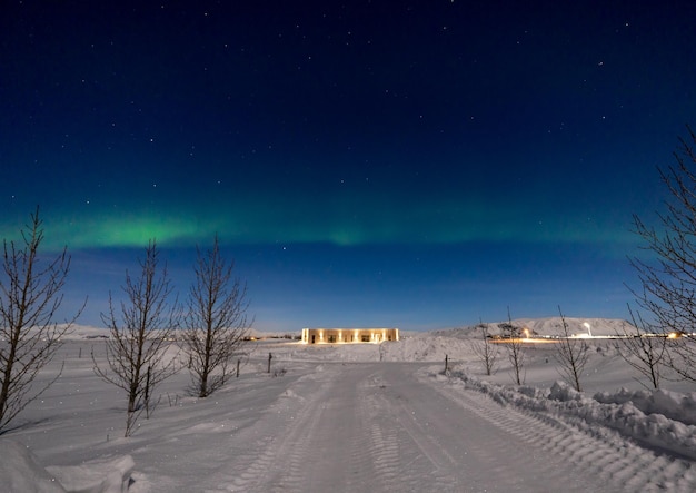 Aurora boreal na linha do horizonte e estrelas com uma estrada totalmente nevada iluminada pelo luar