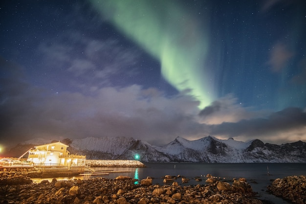 Aurora boreal na montanha nevada com farol em Mefjord Brygge