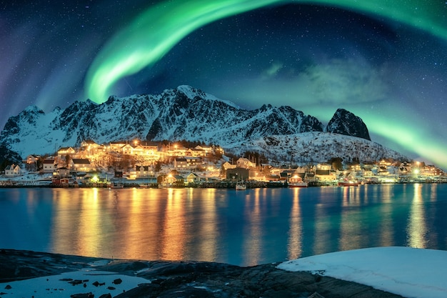 Aurora boreal sobre a iluminação de uma vila de pescadores na costa no inverno nas ilhas lofoten, na noruega