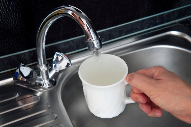 Aus dem Wasserhahn fließt sauberes gefiltertes Wasser. Gefahr durch unbehandeltes Trinkwasser. Wasser in weißes Porzellanglas an der Küchenspüle einfüllen