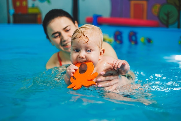 Ausbildung eines Neugeborenen im Pool mit einem Schwimmtrainer Ein Schwimmbad für Babys Kindesentwicklung Ein kleines Kind lernt im Schwimmbad schwimmen