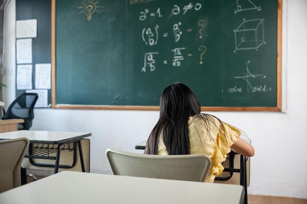 Ausbildung. Rückansicht des Schulmädchens im Unterricht im Klassenzimmer Schreiben Sie fleißig an die Tafel, das Grundschulkind sitzt Unterricht am Tisch in der Schule und schreibt oder zeichnet im Notizbuch, Zurück zum Schulkonzept