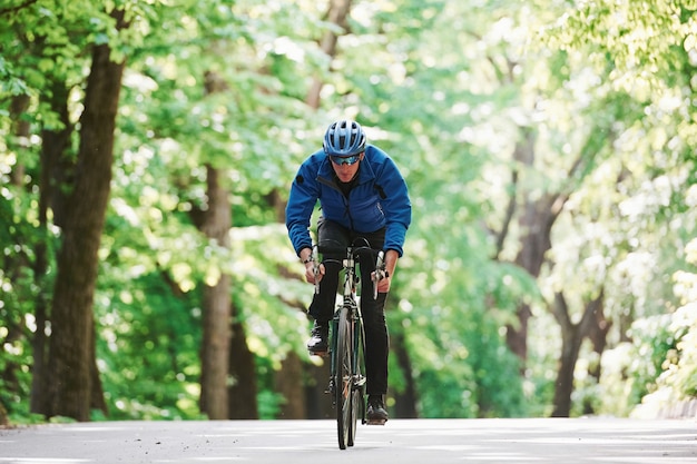 Ausdauer und Kraft. Radfahrer auf einem Fahrrad ist auf der Asphaltstraße im Wald am sonnigen Tag