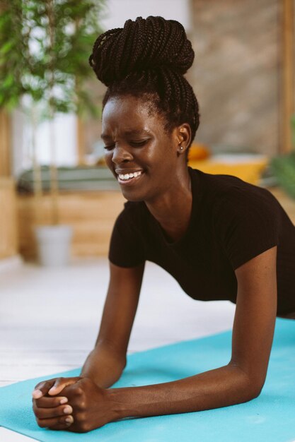 Ausdauernde Afro-Amerikanerin mit Dreadlocks, die durch Schmerzen in der Ellenbogenplanke steht, Nahaufnahmetraining auf Gymnastikmatte im dekorierten Studio