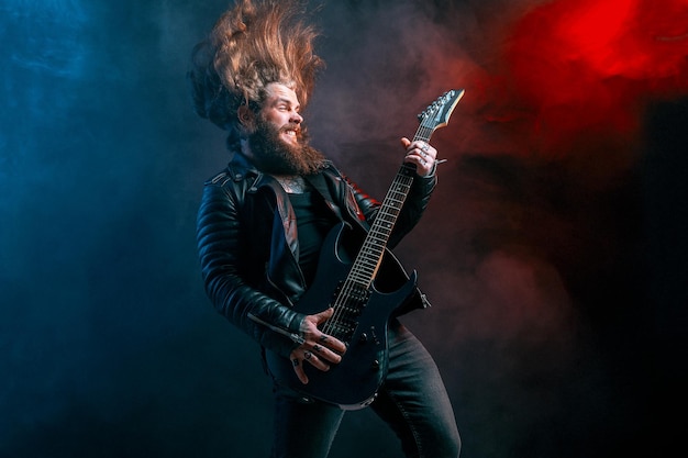 Ausdrucksrock-Gitarrist mit langen Haaren und Bart spielt auf der Studioaufnahme des Rauchhintergrunds