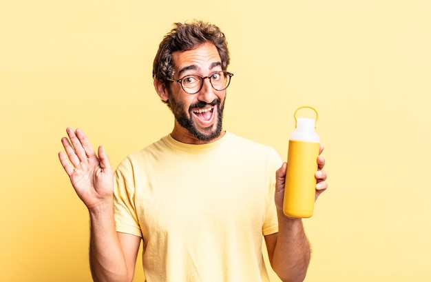 ausdrucksstarker verrückter Mann, der glücklich lächelt, die Hand winkt, Sie mit einer Tee-Thermosflasche begrüßt und begrüßt