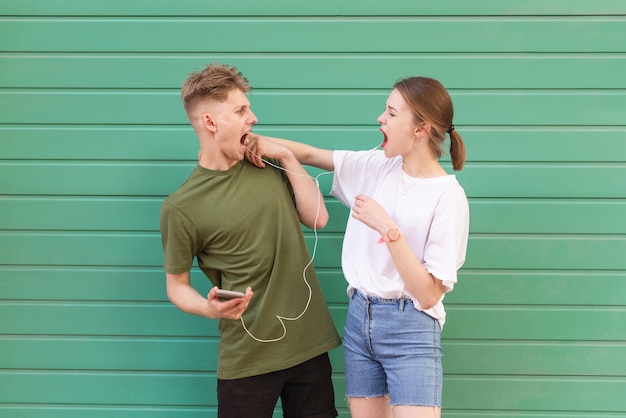 Foto ausdrucksstarkes amüsantes paar, das musik in kopfhörern auf einem grün hört