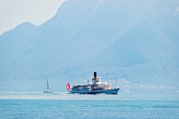 Ausflugsschiff mit Schweizer Flagge auf dem Genfersee am Ouchy-Damm in Lausanne, Schweiz. Leute an Bord