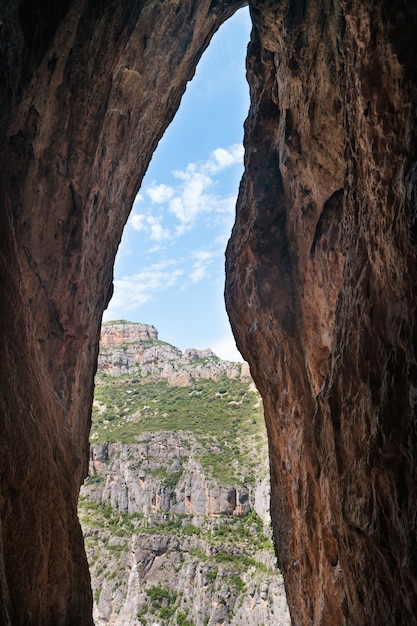 Ausgang aus der Höhle zu sonniger Landschaft mit Wald und blauem Himmel