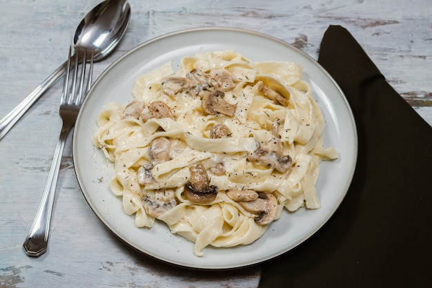 Foto ausgefallene bio-fetuccine-nudeln mit cremiger alfredo-pilzsauce. rustikale oberfläche.