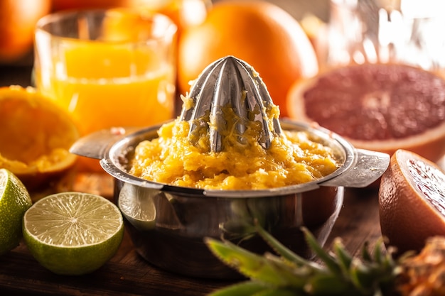 Ausgepresstes Orangenmark in einem Entsafter mit frisch geschnittenen Zitrusfrüchten und einem Glas Saft.