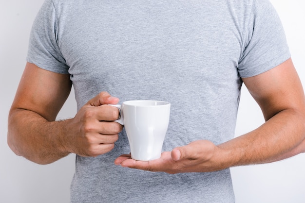 Ausgeschnittene Ansicht des gutaussehenden Mannes, der steht und eine Tasse Morgentee oder Kaffee hält, während er vor der Kamera posiert. Stock Foto