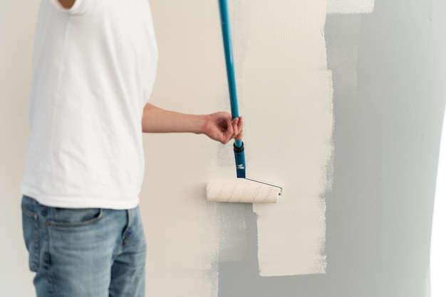 Foto ausgeschnittene ansicht des kaukasischen mannes, der wände streicht, während er die farbrolle schmutzig von der farbe hält. männlicher umbau seiner neuen wohnung