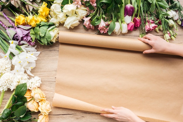 Ausgeschnittene Ansicht eines Floristen mit Bastelpapier und bunten Blumen auf Holzoberfläche