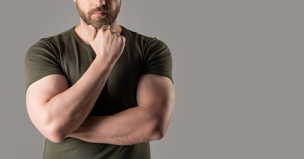Ausgeschnittene Ansicht eines muskulösen Mannes im T-Shirt. Muskulöser Mann isoliert auf grauem Hintergrund mit Kopierraum. Muskulöser Mann im Studio. Foto eines muskulösen Mannes mit verschränkten Händen