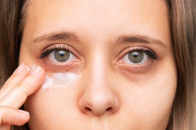 Ausgeschnittene Aufnahme einer jungen Frau, die eine Gesichtshaut berührt, während sie die Creme für schwarze Augen aufträgt