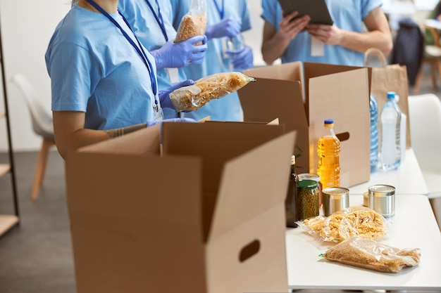 Ausgeschnittene Aufnahme von Freiwilligen in Schutzhandschuhen, die Lebensmittel in Kartons sortieren, die daran arbeiten
