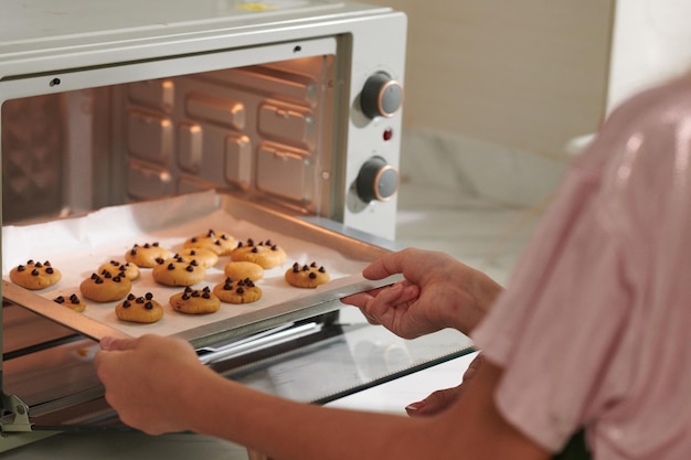 Ausgeschnittenes Bild einer Frau, die ein Tablett mit Schokoladenkeksen in den Ofen stellt