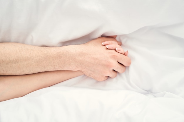 Ausgeschnittenes Foto des leidenschaftlichen kaukasischen frisch verheirateten Paares, das sich gegenseitig die Hände im Bett hält