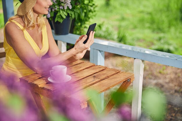 Ausgeschnittenes Foto einer glücklichen blonden kaukasischen Dame mit Hut, die am Tisch sitzt