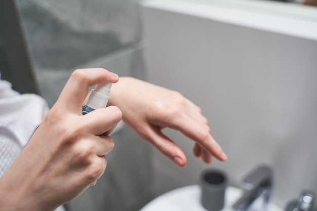 Ausgeschnittenes Foto einer jungen kaukasischen Frau, die ein antiseptisches Spray zur wirksamen Hautdesinfektion anwendet