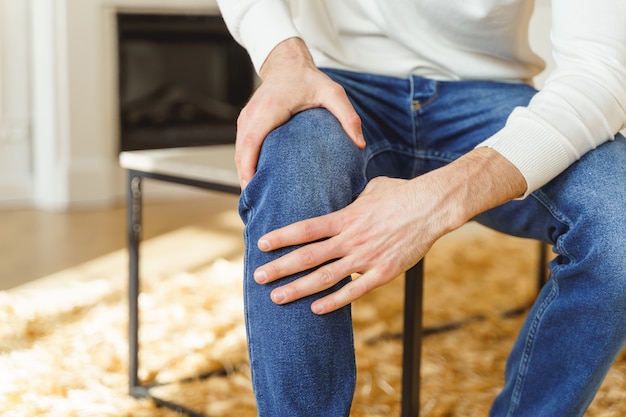 Ausgeschnittenes Foto eines sitzenden jungen Mannes, der im Büro an Gelenkschmerzen leidet