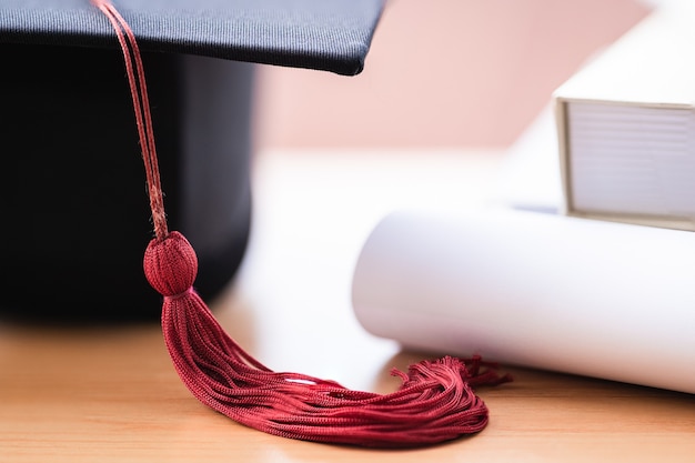 Ausgeschnittenes Foto eines Universitätsabschlusshutes und Diplomabschlusszeugnisses auf dem Tisch