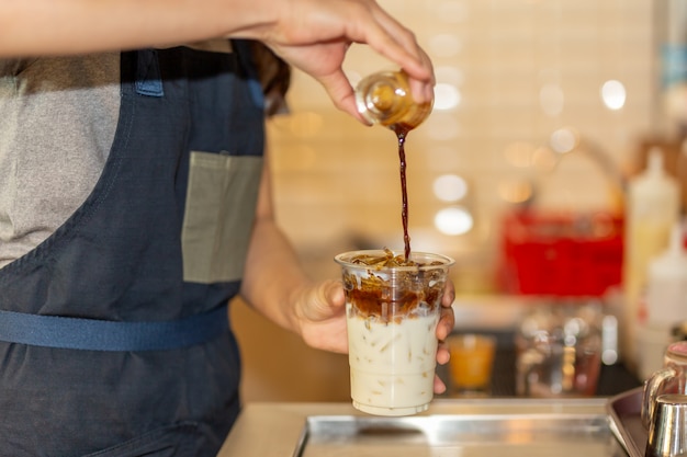 Auslaufender Kaffee Barista zur Mitnehmerschale zur Herstellung von Eiskaffee Latte im Café.