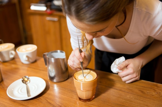 Ausrüstung, Café, Menschen und Technologiekonzept - Nahaufnahme einer Frau, die Sahne in eine Tasse Kaffee in einer Cafébar oder Restaurantküche gießt