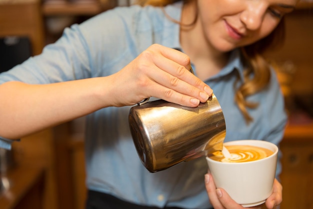 Ausrüstung, Café, Menschen und Technologiekonzept - Nahaufnahme einer Frau, die Sahne in eine Tasse Kaffee in einer Cafébar oder Restaurantküche gießt