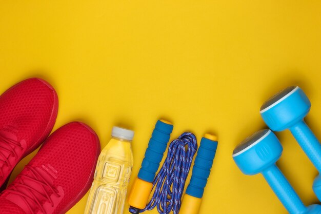 Ausrüstung für das training auf gelbem hintergrund. sportschuhe, springseil, hanteln, flasche wasser. flacher laienstil.