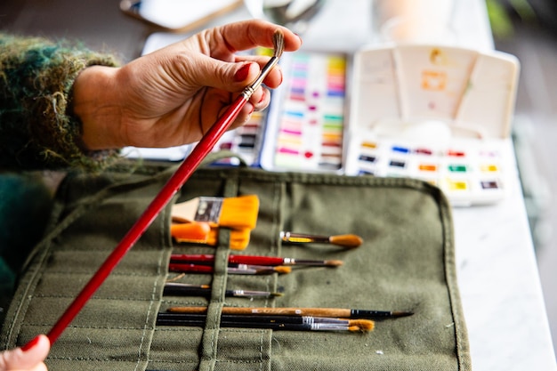 Ausschnitt der Hand einer Frau, die einen Aquarellpinsel aus ihrem Materialbeutel berührt