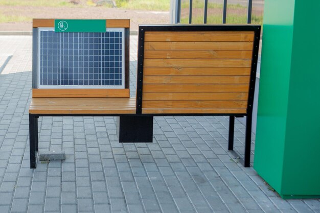 Außenaufnahme einer Holzbank im Park mit installiertem Solarpanel USB-Kabel mit Smartphone verbunden