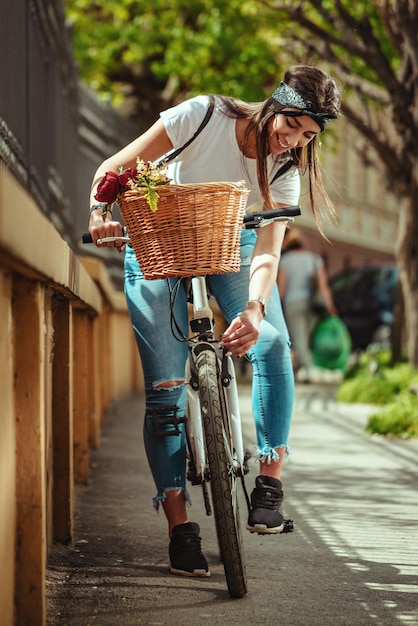 Außenaufnahme einer jungen Frau, die mit dem Fahrrad entlang der Stadtstraße fährt und das Rad des Fahrrads überprüft.