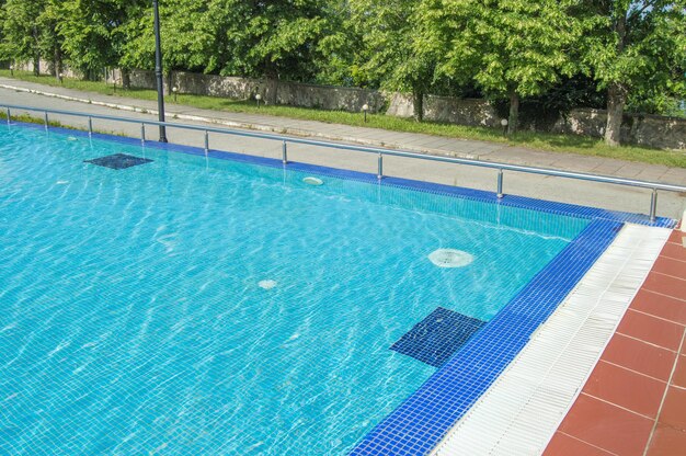 Außenpool mit blauem Wasser auf einem Hintergrund von Bäumen an einem sonnigen Sommertag im Freien