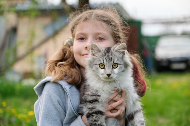 Außenporträt des Mädchenkindes, das in ihren Armen geliebtes Haustier flauschige graue Katze hält
