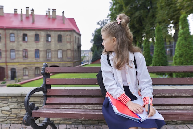 Außenporträt des schönen Mädchens mit dem Rucksack, der in Notizbuch schreibt