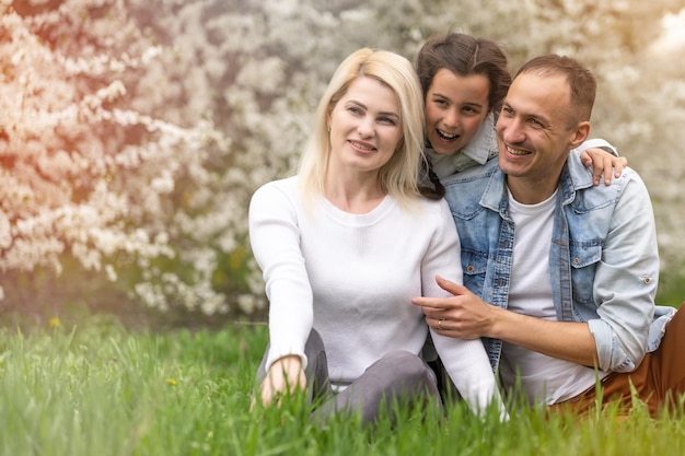 Außenporträt einer glücklichen jungen Familie, die im Frühlingspark unter blühendem Baum spielt, schöne Familie, die sich im sonnigen Garten amüsiert