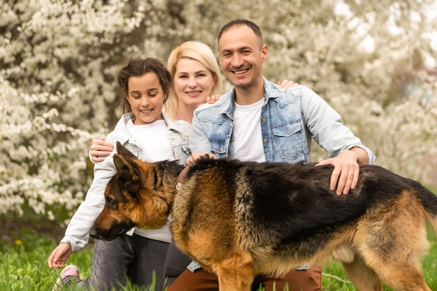 Außenporträt einer glücklichen jungen Familie, die im Frühlingspark unter blühendem Baum spielt, schöne Familie, die sich im sonnigen Garten amüsiert