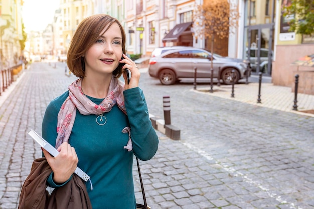 Außenporträt einer jungen Frau, die die Straße hinuntergeht und am Telefon spricht Lifestyle