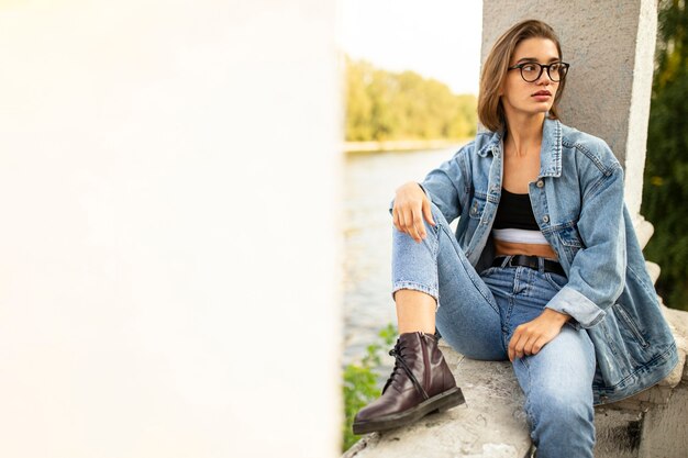 Außenporträt einer jungen jungen Hipster-Frau, gekleidet in Jeans und Stiefeln, draußen sitzend