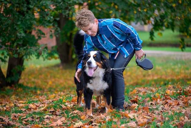 Außenporträt eines Jungen mit Berner Berghund im Herbst Freundschaft eines Teenagers mit Haustier