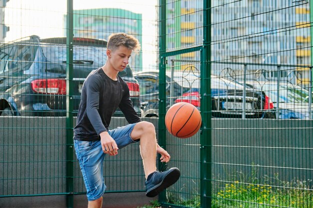 Außenporträt eines Teenagers, der Straßenbasketball spielt. Aktiver gesunder Lebensstil, Hobbys und Freizeit, Jugendkonzept