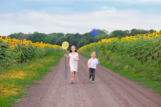 Außenporträt von kleinen Kindern, die mit einem Schmetterlingsnetz entlang der Straße laufen.