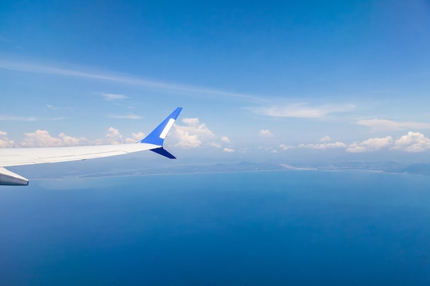 Aussicht aus dem Fenster des Flugzeugs auf dem Flügel vor dem Hintergrund des blauen Meeres, des Himmels und der Küste der Insel Reisen und Urlaub