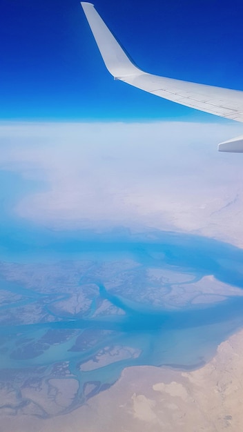 Aussicht aus dem Flugzeugfenster auf den blauen Himmel und die Erde mit der Landschaft der Wüste Meer und Kanäle in