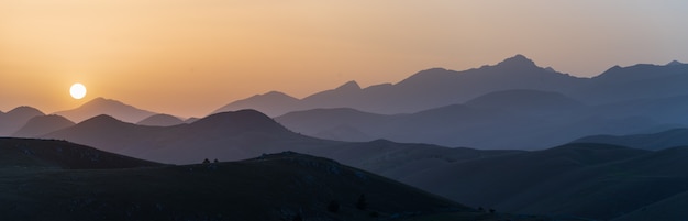 Aussichtspunkt für den Sonnenuntergang auf der Silhouette der felsigen Berge. Campo Imperatore, Gran Sasso, Apennin, Italien. Die Sonne des klaren Himmels platzte auf einem dramatischen Bergkamm.