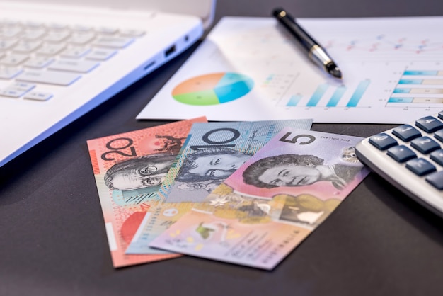 Australische Dollar-Banknoten, Laptop und Diagramm auf schwarzem Tisch